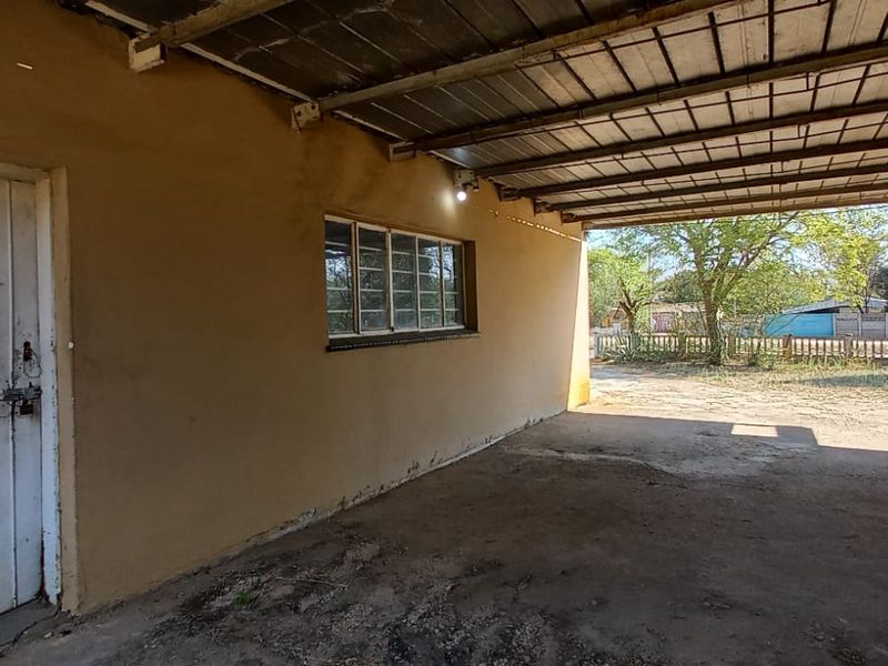 A covered outdoor patio area featuring a corrugated metal roof, concrete flooring, and direct access to the rear garden space.