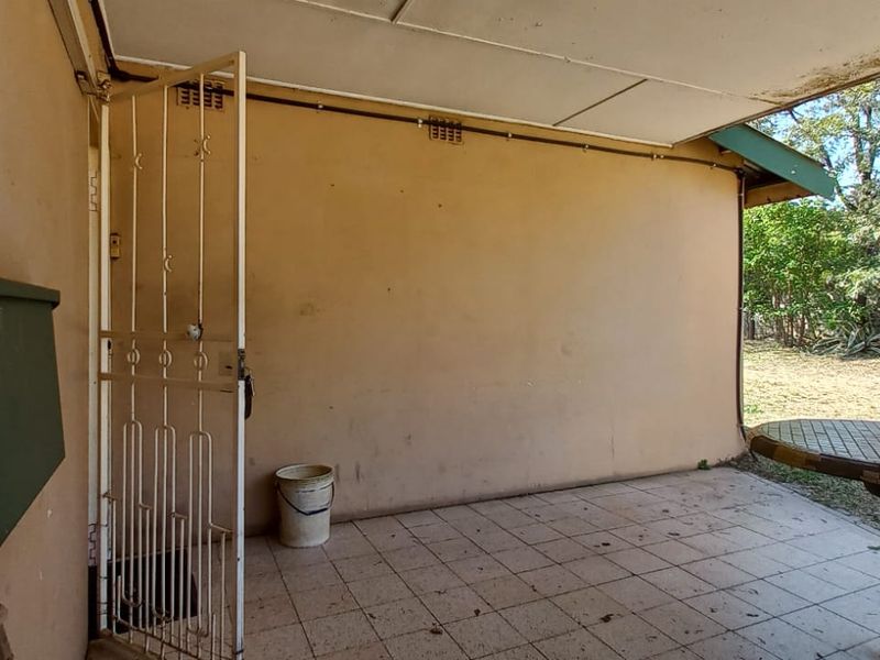 A covered outdoor patio area featuring tiled flooring, a built-in table, and a security gate, requiring some maintenance and cosmetic updates.