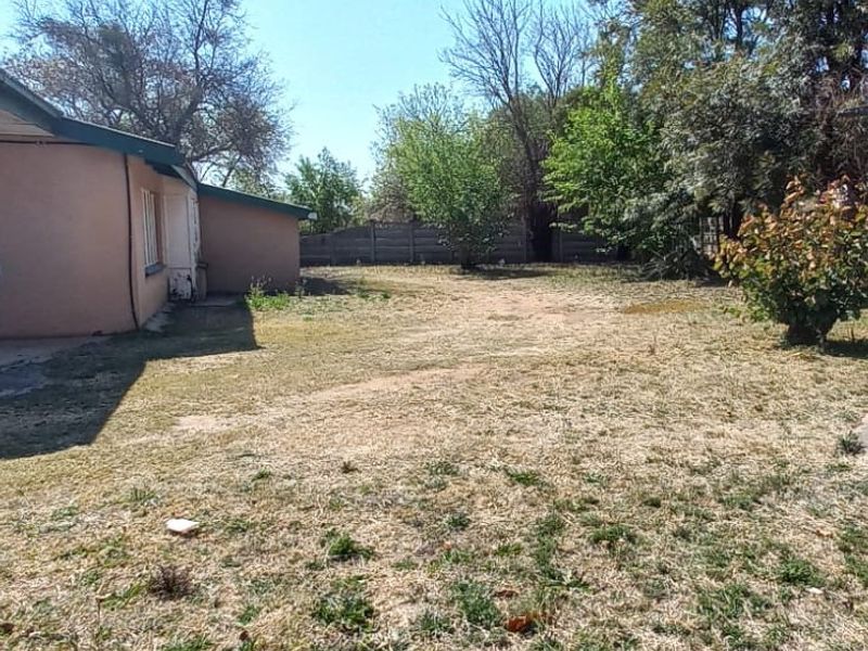 A spacious rear garden area featuring a large lawn, mature trees, and a precast concrete boundary wall, offering potential for landscaping.
