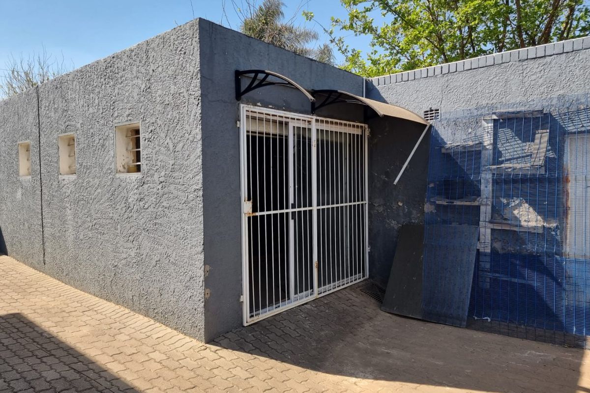 Rear exterior view of a commercial building featuring a textured facade, security gate, and a small entrance awning over a paved area.