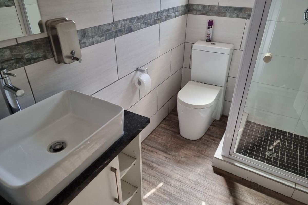 A modern bathroom featuring a vessel sink on a vanity cabinet, a toilet, and a glass-enclosed shower with tiled walls and wood-look flooring.