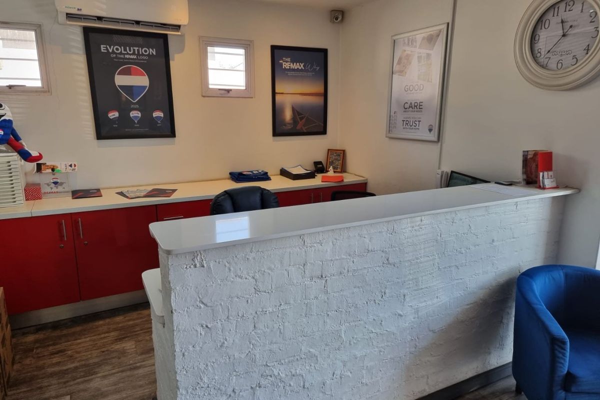A functional commercial office reception area featuring a white brick-fronted desk, built-in red cabinetry, and a wall-mounted air conditioning unit.