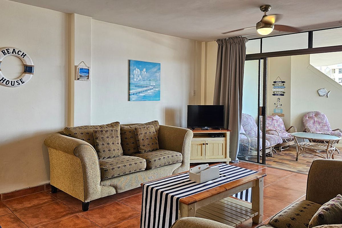 A comfortable living room featuring tiled flooring, a ceiling fan, and large sliding glass doors that provide access to an outdoor patio area.