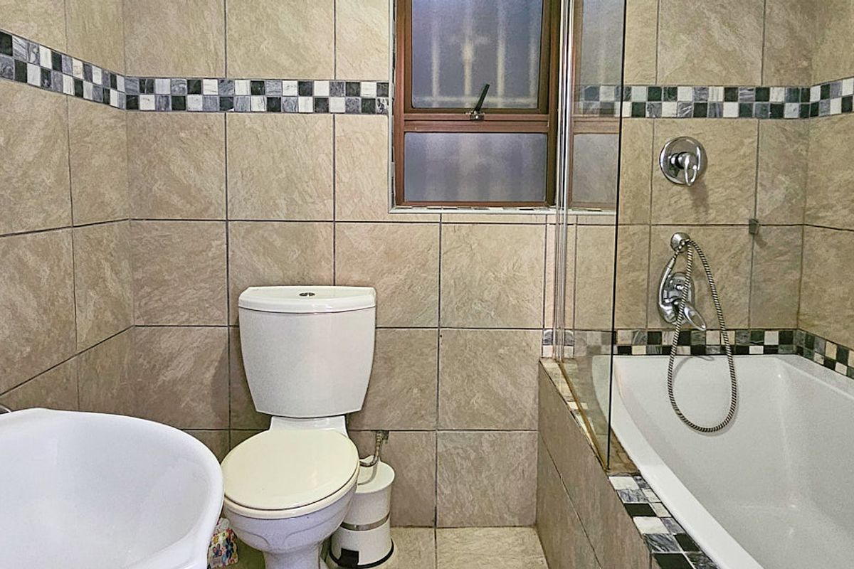 A functional bathroom featuring a bathtub with a shower mixer, glass screen, and neutral tiled walls with a decorative mosaic border.