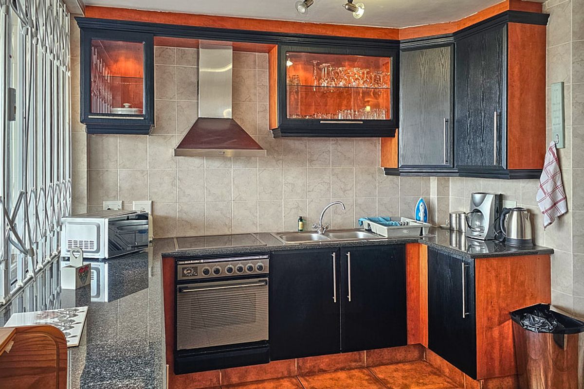 A functional kitchen featuring dark wood cabinetry, granite countertops, a built-in oven with hob, and a stainless steel extractor fan.