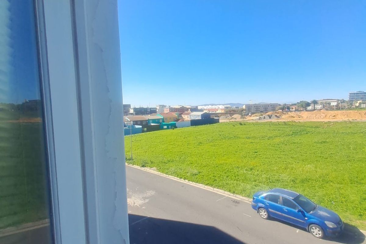 An elevated view from a window overlooking a street and open green field, showing visible wear on the window frame paint.