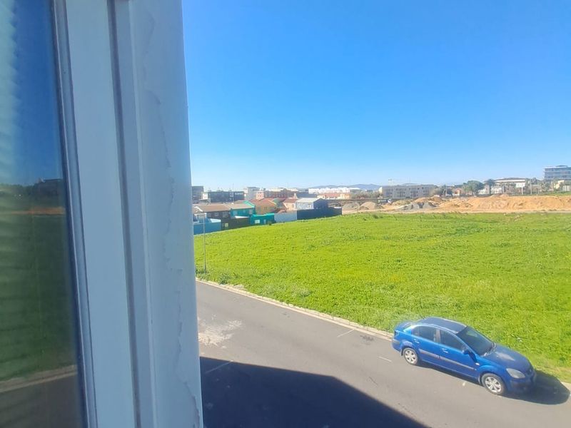 An elevated view from a window overlooking a street and open green field, showing visible wear on the window frame paint.