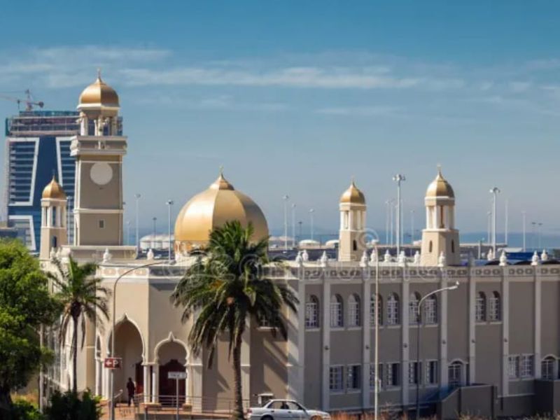 An exterior view of a large building with golden domes and architectural detailing, situated in an urban environment.