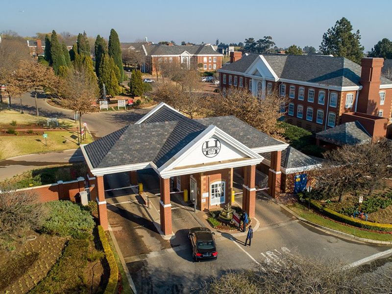 Aerial view of a commercial office park entrance featuring a brick security gatehouse, landscaped grounds, and multiple multi-story office buildings.