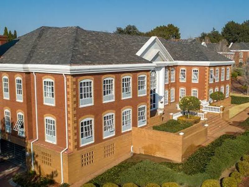 Aerial view of a multi-story commercial brick building featuring a pitched roof, extensive casement windows, and landscaped terraced gardens with retaining walls.