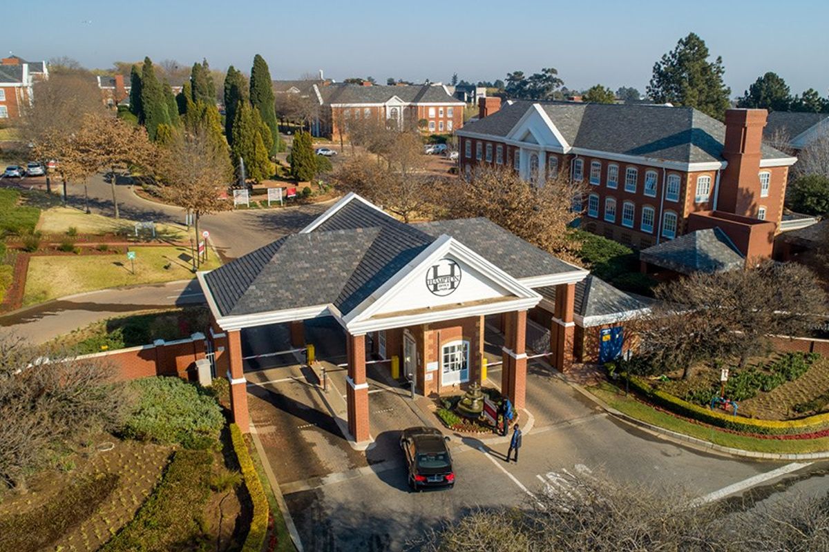 Aerial view of a commercial office park entrance featuring a brick security gatehouse, landscaped grounds, and multiple multi-story office buildings.