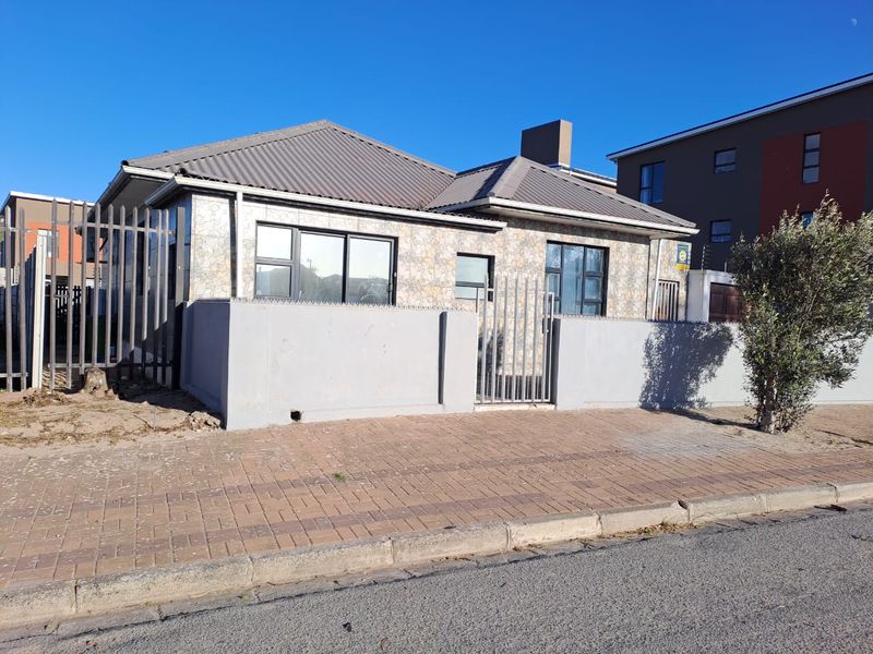 Front view of a single-story house featuring stone cladding, a metal roof, and secure perimeter walling with metal fencing.