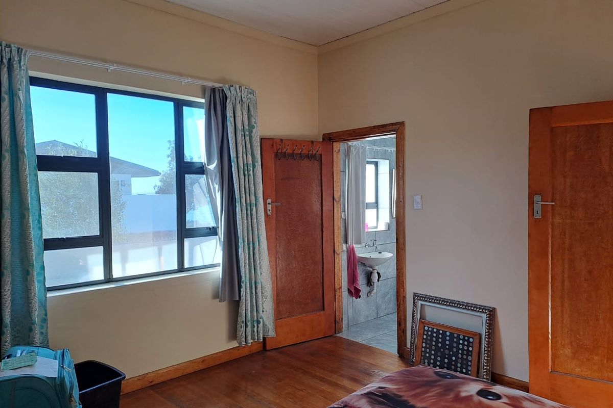 A bedroom featuring timber flooring, aluminium window frames, and direct access to an en-suite bathroom with tiled finishes.