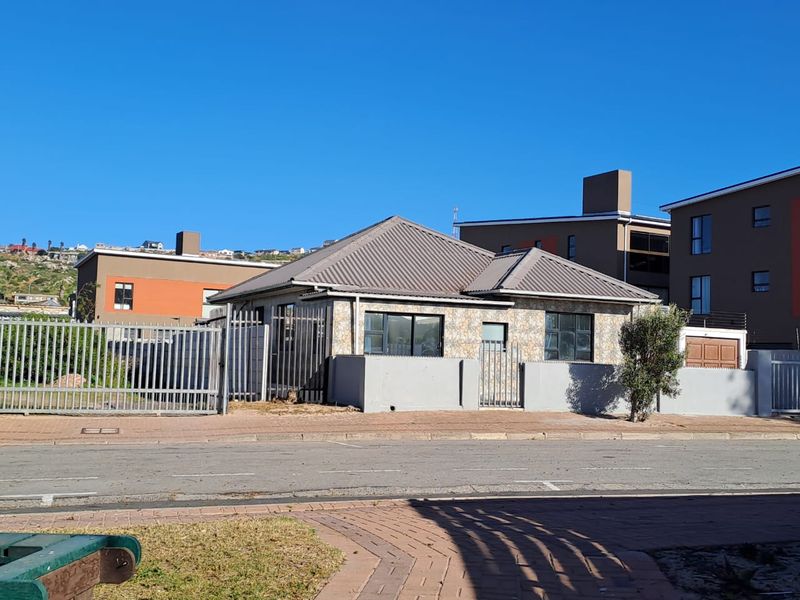 Front view of a single-story house featuring stone cladding, a metal roof, and secure perimeter fencing with a paved driveway.
