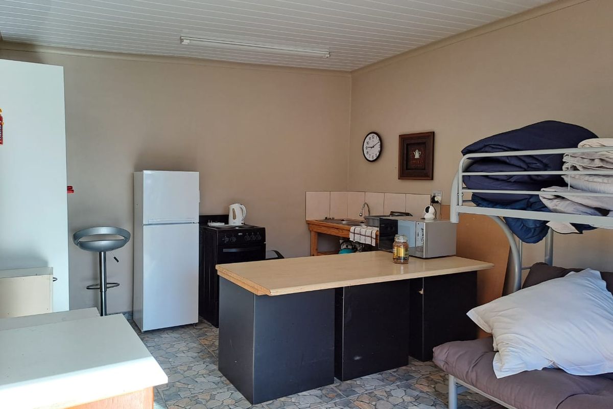 A compact kitchen area featuring a basic sink, tiled splashback, and freestanding stove, with a functional layout and dated finishes.