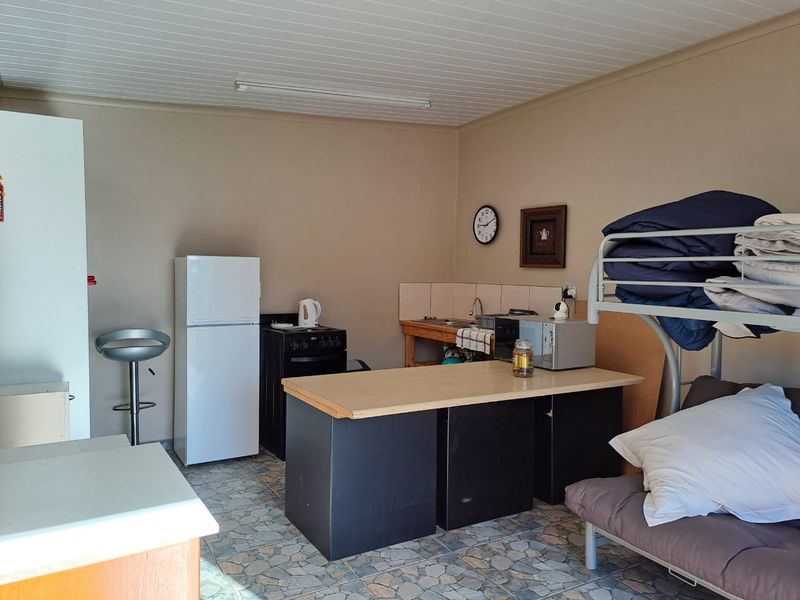 A compact kitchen area featuring a basic sink, tiled splashback, and freestanding stove, with a functional layout and dated finishes.