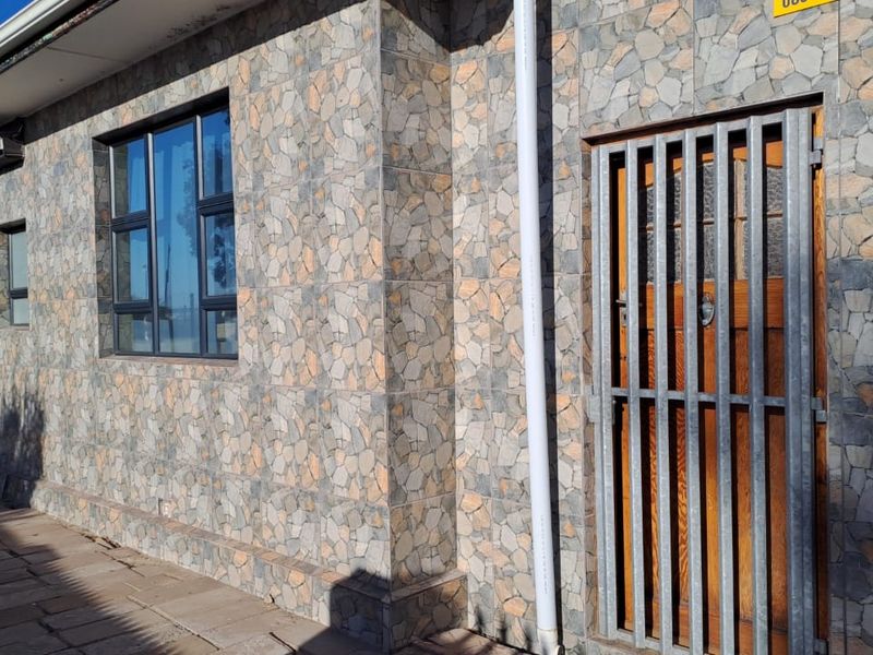 Exterior view of the property featuring stone cladding, aluminium window frames, and a secure metal entrance gate.