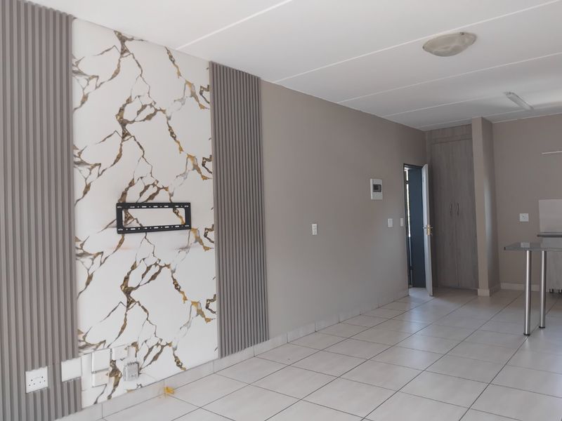 An open-plan living area featuring a modern marble-effect feature wall with slatted paneling, tiled flooring, and a built-in storage cupboard.