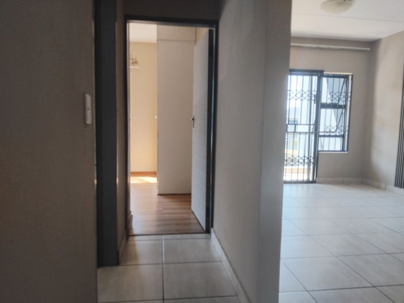 A view through a hallway connecting to an open living area, featuring tiled floors and security fixtures on windows and doors.