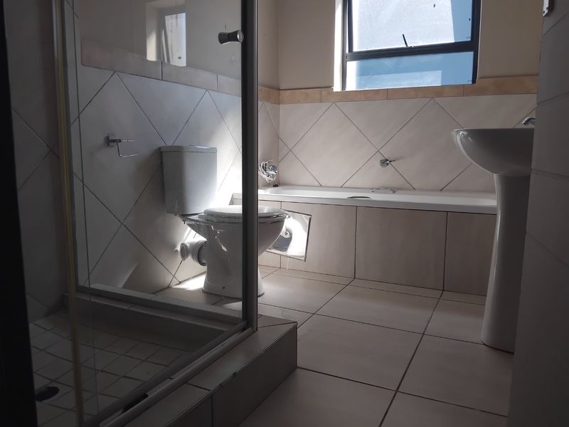A functional bathroom featuring a shower enclosure, bathtub, toilet, and pedestal basin with neutral wall and floor tiling.
