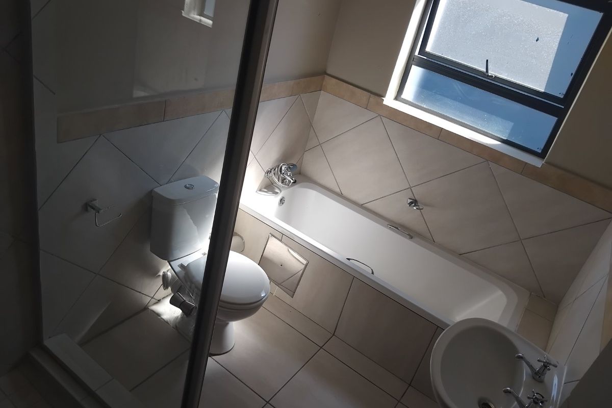 A clean, functional bathroom featuring a bathtub, separate shower enclosure, pedestal basin, and neutral wall and floor tiling.