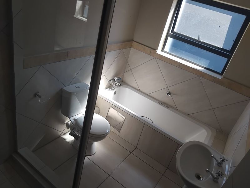 A clean, functional bathroom featuring a bathtub, separate shower enclosure, pedestal basin, and neutral wall and floor tiling.