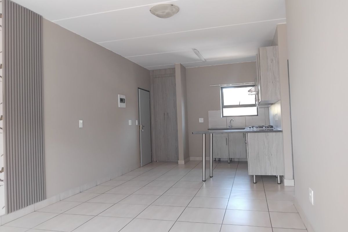 An open-plan living and kitchen area featuring neutral tones, tiled flooring, built-in cabinetry, and a functional kitchen layout.