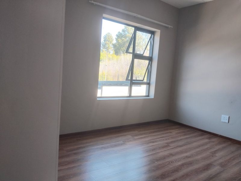A bright, empty bedroom featuring modern laminate flooring and a large aluminium-framed window with natural light.