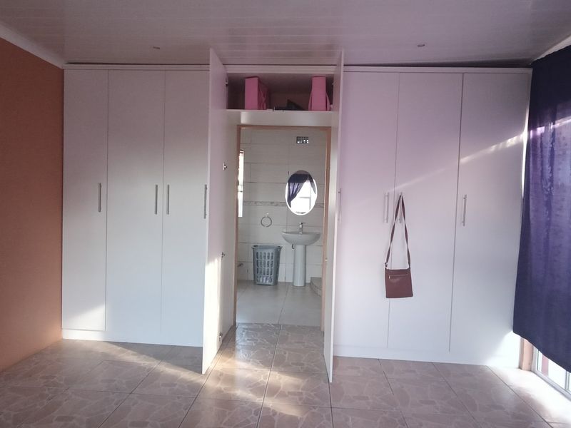 A bedroom featuring extensive built-in cupboards and tiled flooring, with a direct view into an adjoining en-suite bathroom.