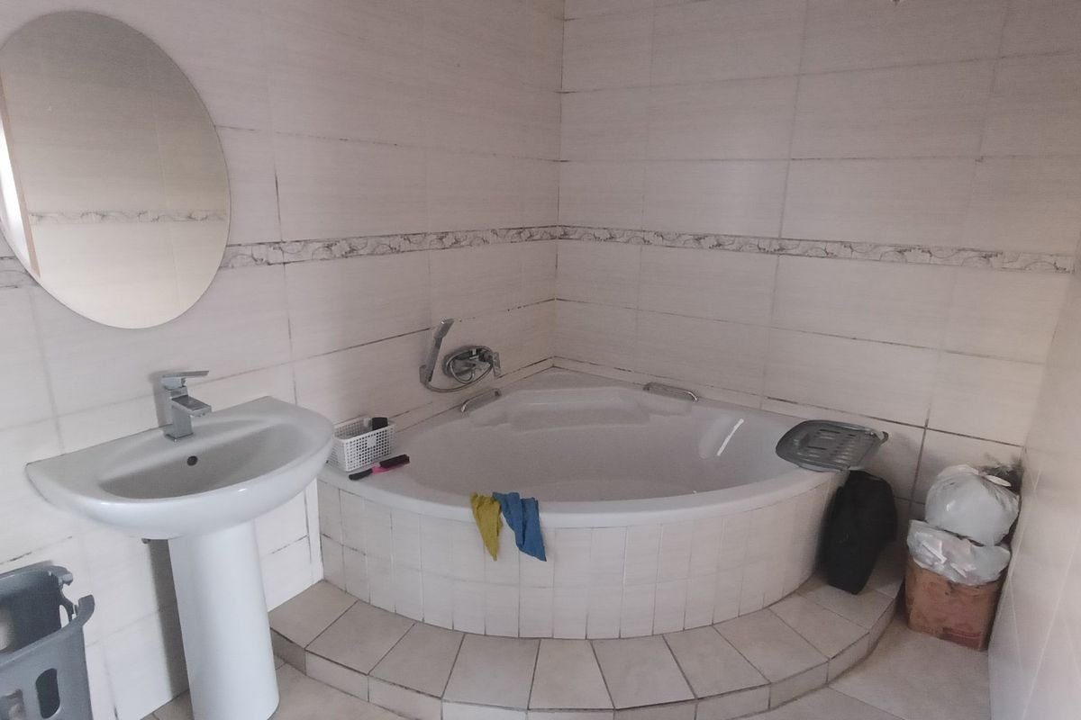 A functional bathroom featuring a corner bathtub, pedestal basin, and neutral wall tiling. The space offers a practical layout with potential for modern updates.