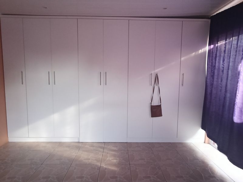 A bedroom featuring extensive floor-to-ceiling built-in cupboards and tiled flooring, offering ample storage space.