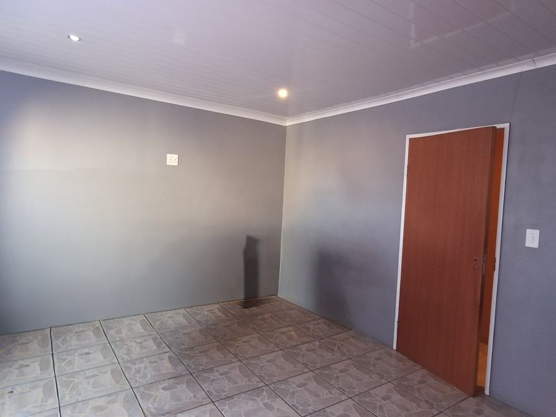 An empty bedroom featuring grey painted walls, tiled flooring, and recessed ceiling lighting, ready for personalization.