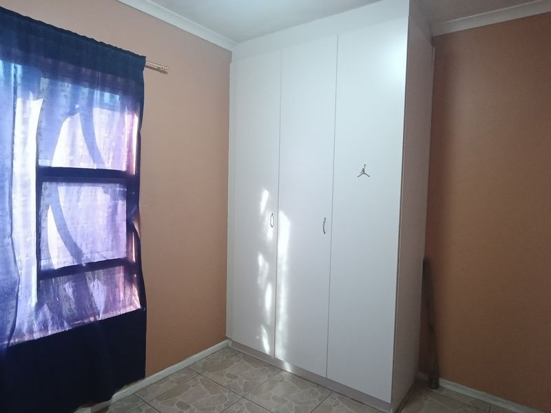 A bedroom featuring tiled flooring and a white built-in wardrobe with three doors.