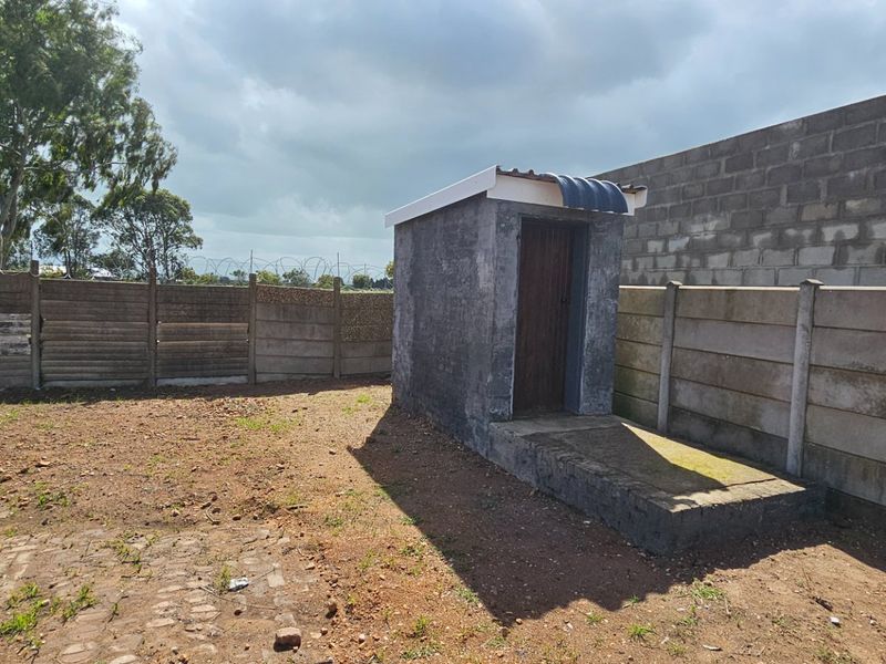 Rear exterior area featuring a small utility structure, enclosed by a precast concrete boundary wall with security razor wire.