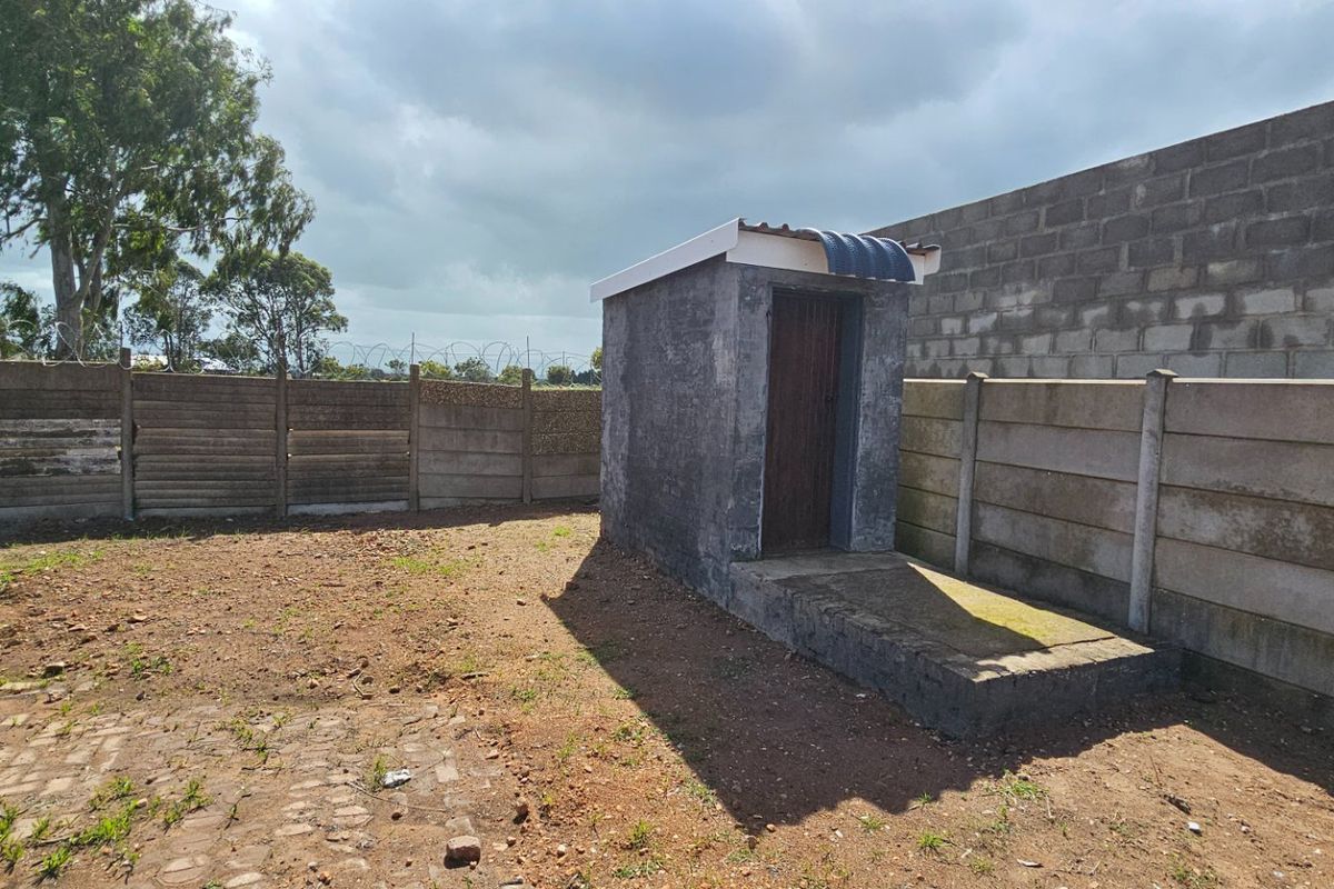 Rear yard area featuring a small utility structure, enclosed by precast concrete boundary walls with security razor wire and paved ground surfaces.