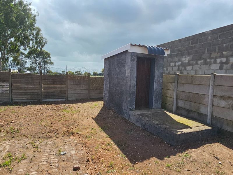 Rear yard area featuring a small utility structure, enclosed by precast concrete boundary walls with security razor wire and paved ground surfaces.