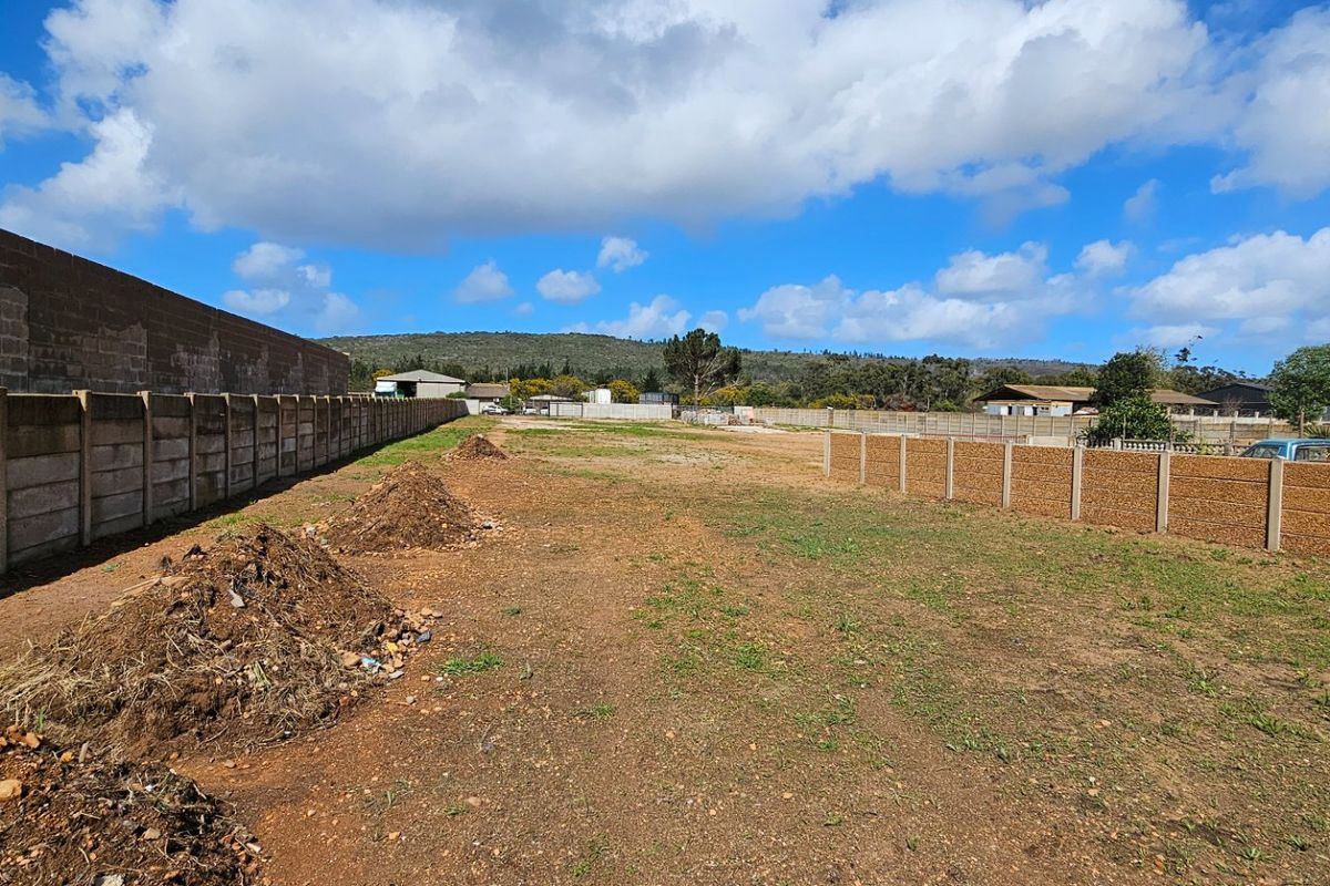 A large, undeveloped industrial plot featuring perimeter precast concrete boundary walls and open, unpaved ground.