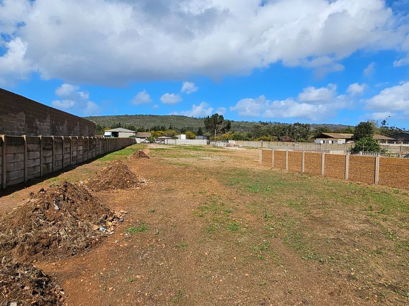A large, undeveloped industrial plot featuring perimeter precast concrete boundary walls and open, unpaved ground.