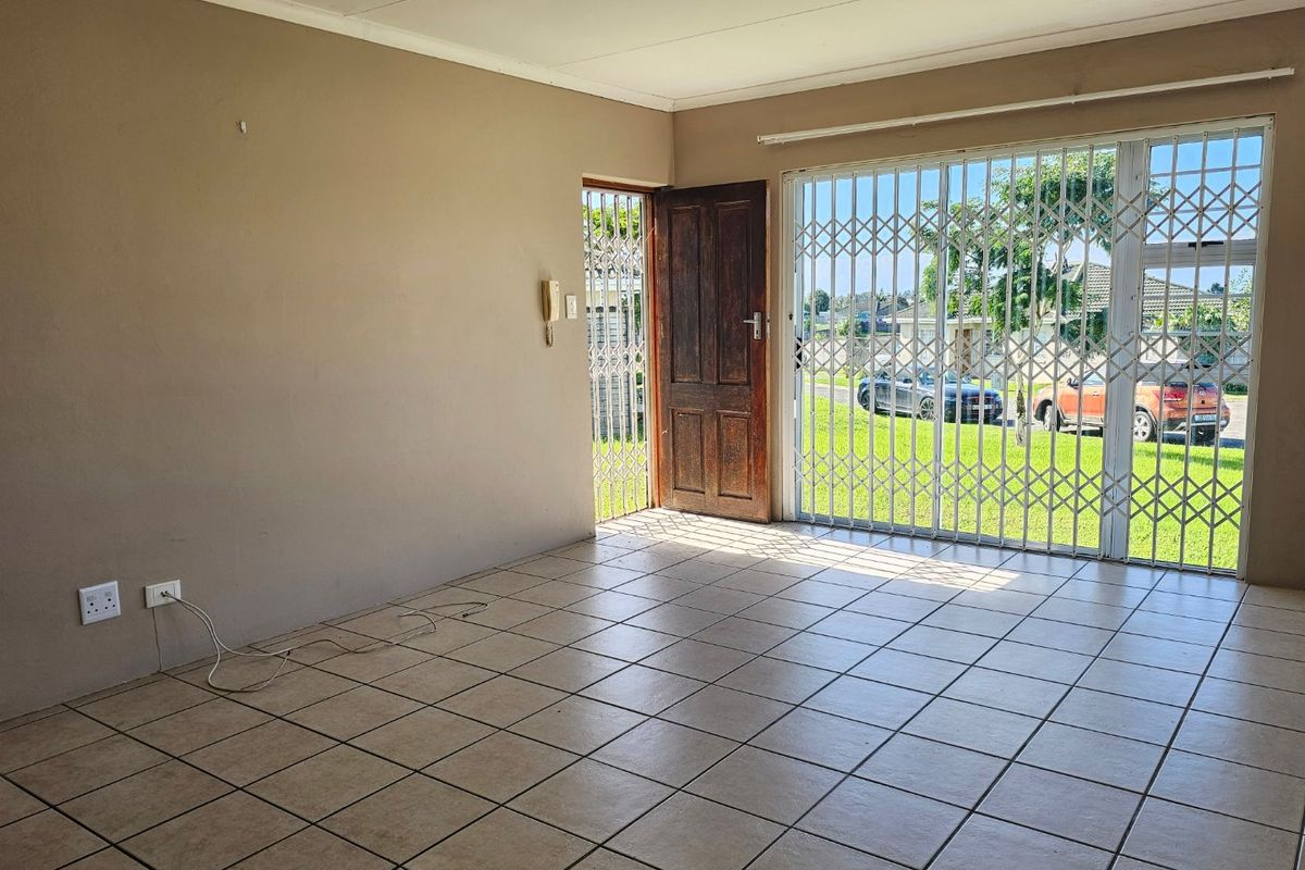 An empty living room featuring tiled flooring, a security gate, and a sliding door providing access to the exterior.