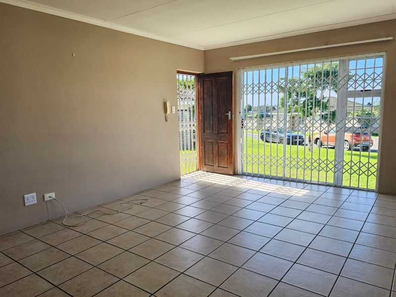 An empty living room featuring tiled flooring, a security gate, and a sliding door providing access to the exterior.