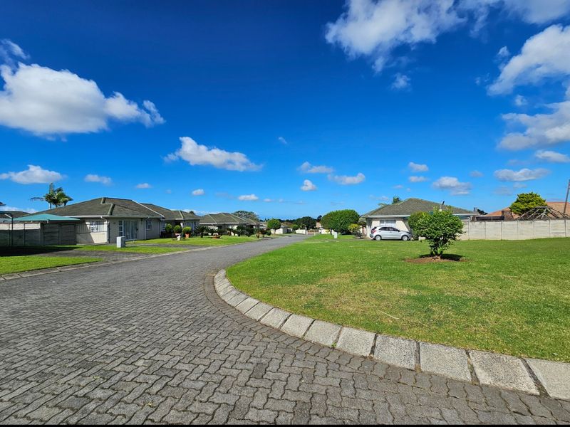 A view of the residential street within the townhouse complex, featuring paved driveways, landscaped lawns, and established residential units.