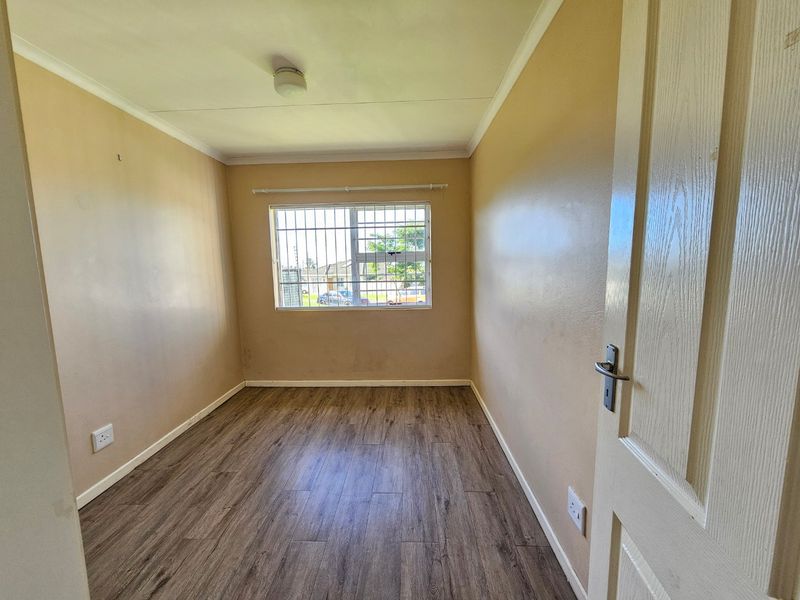 An empty bedroom featuring laminate flooring, neutral wall paint, and a window fitted with security bars.