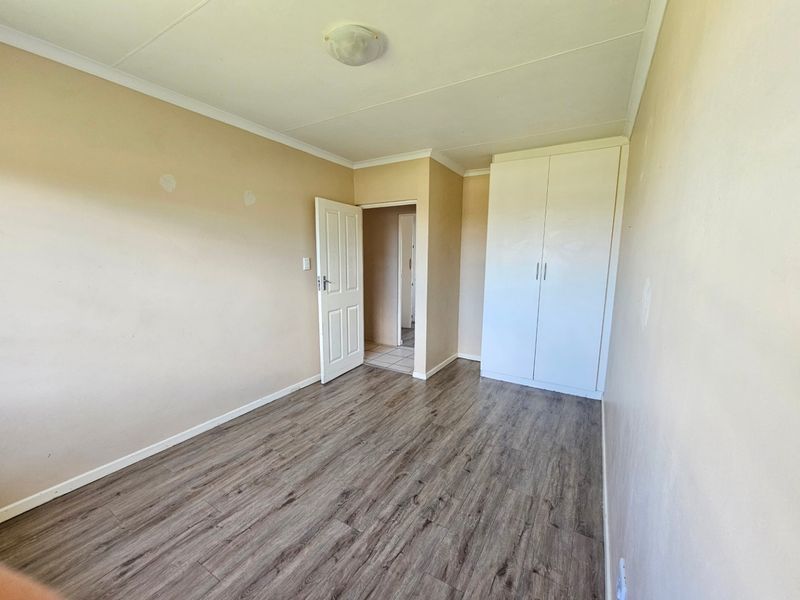 An empty bedroom featuring laminate flooring, a built-in wardrobe, and neutral wall finishes, ready for personalization.
