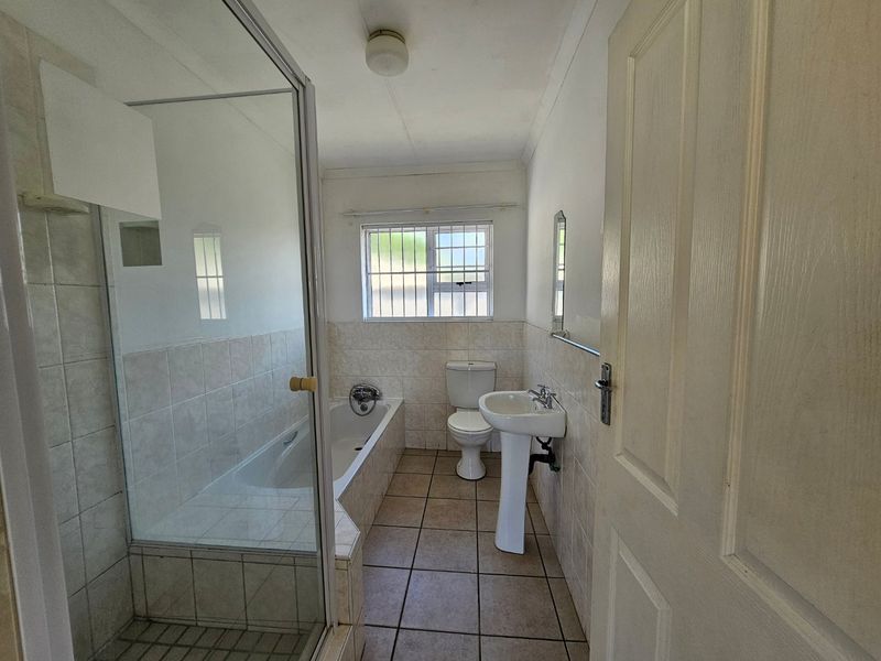 A functional bathroom featuring a separate shower enclosure, bathtub, pedestal sink, and toilet with neutral tiled finishes.