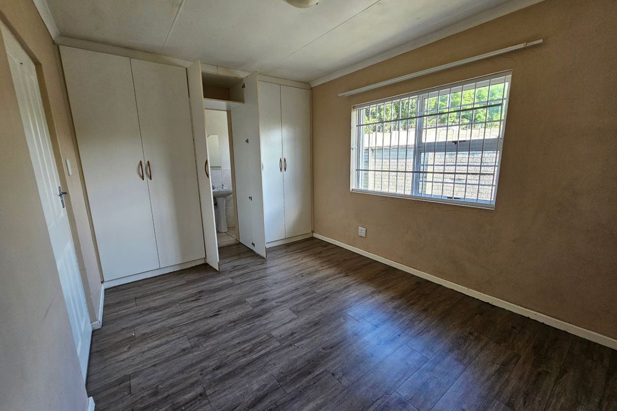 A vacant bedroom featuring laminate flooring, built-in cupboards, and a window with security bars, offering a blank canvas for personalization.