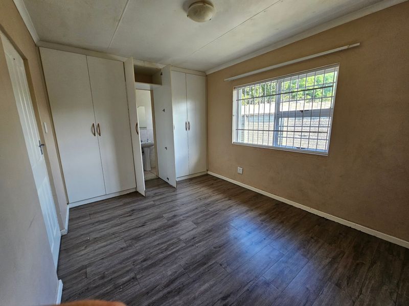 A vacant bedroom featuring laminate flooring, built-in cupboards, and a window with security bars, offering a blank canvas for personalization.