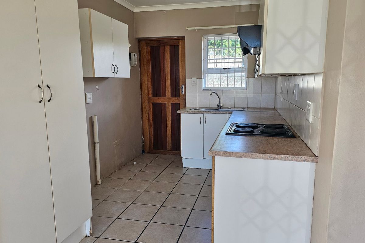 A functional kitchen featuring built-in cabinetry, laminate countertops, an electric hob, and tiled flooring, offering a blank canvas for potential modern updates.