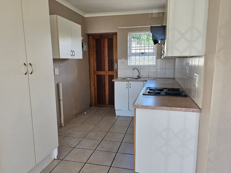 A functional kitchen featuring built-in cabinetry, laminate countertops, an electric hob, and tiled flooring, offering a blank canvas for potential modern updates.