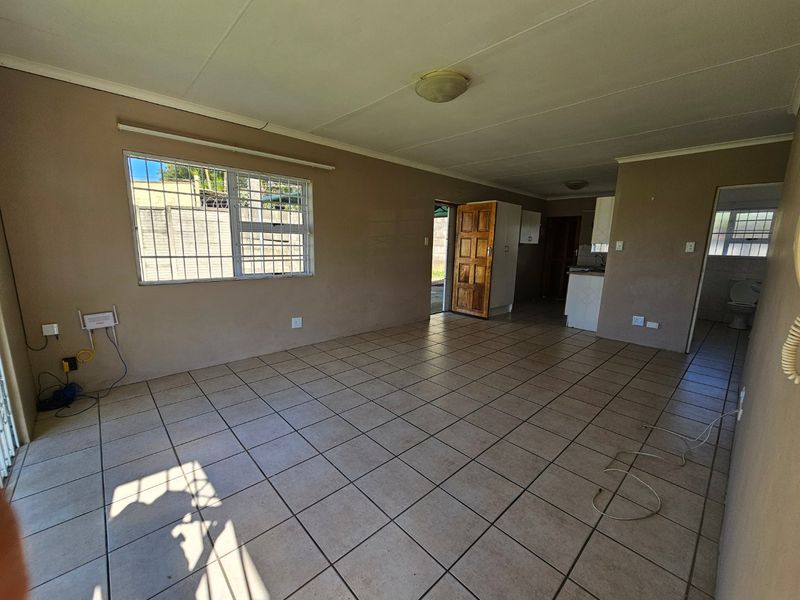 An open-plan living and kitchen area featuring tiled flooring, security bars on windows, and neutral wall tones, offering a blank canvas for renovation.