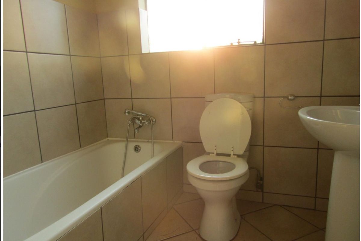 A functional bathroom featuring a bathtub, pedestal basin, and toilet with neutral wall and floor tiling.